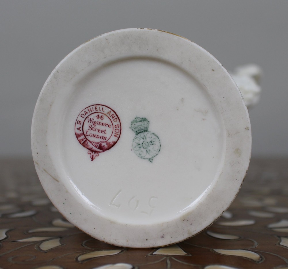 A white porcelain vase featuring gilded scrollwork, dolphin handles, mascaron side mounts, and a central cameo medallion depicting a cherub. View VII