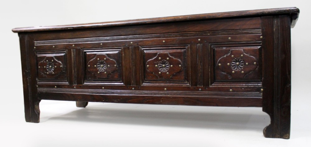 A low rectangular dark oak coffer with a plank lid and four carved recessed panels accented with brass studs. View V