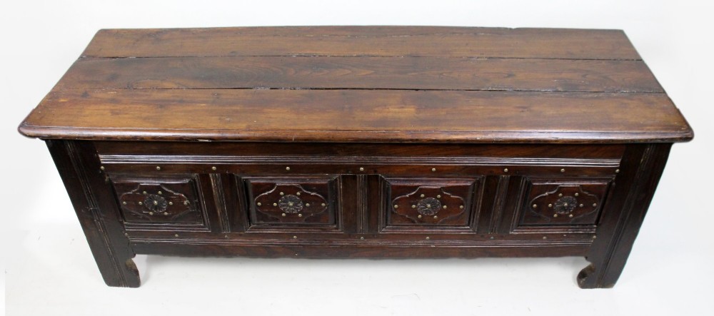 A low rectangular dark oak coffer with a plank lid and four carved recessed panels accented with brass studs. View VI