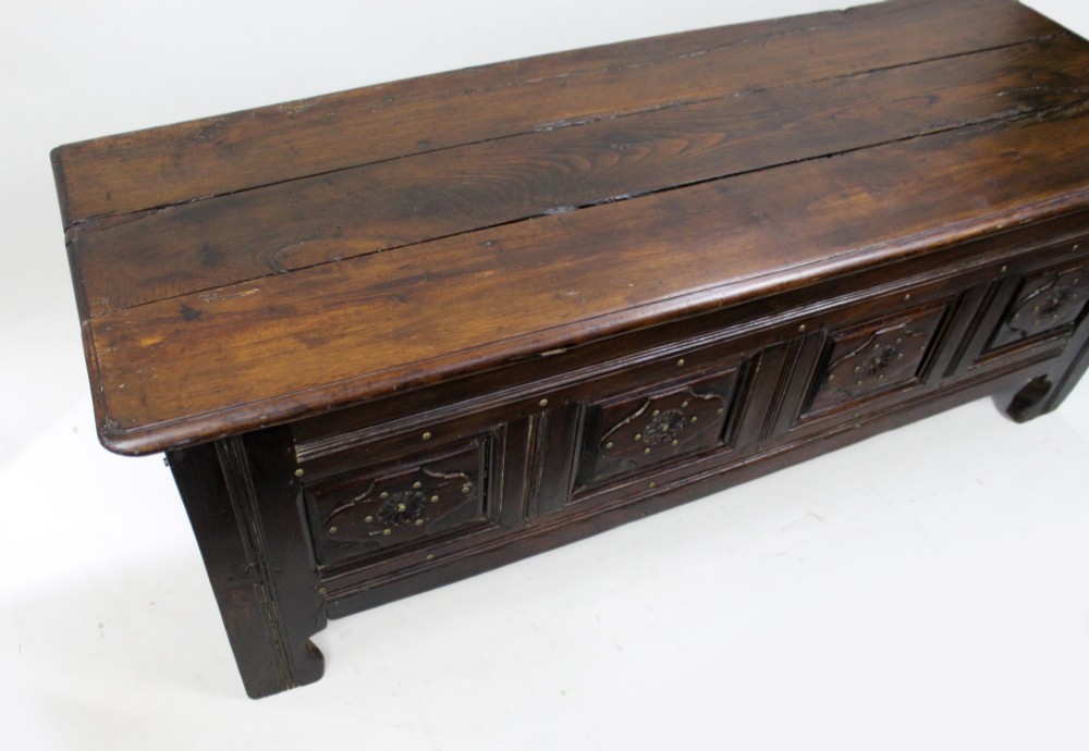 A low rectangular dark oak coffer with a plank lid and four carved recessed panels accented with brass studs. View VII