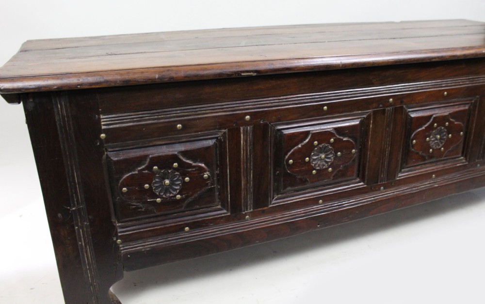 A low rectangular dark oak coffer with a plank lid and four carved recessed panels accented with brass studs. View VIII