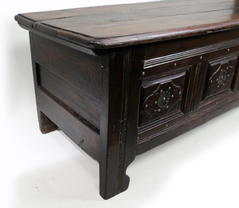 A low rectangular dark oak coffer with a plank lid and four carved recessed panels accented with brass studs. View IX