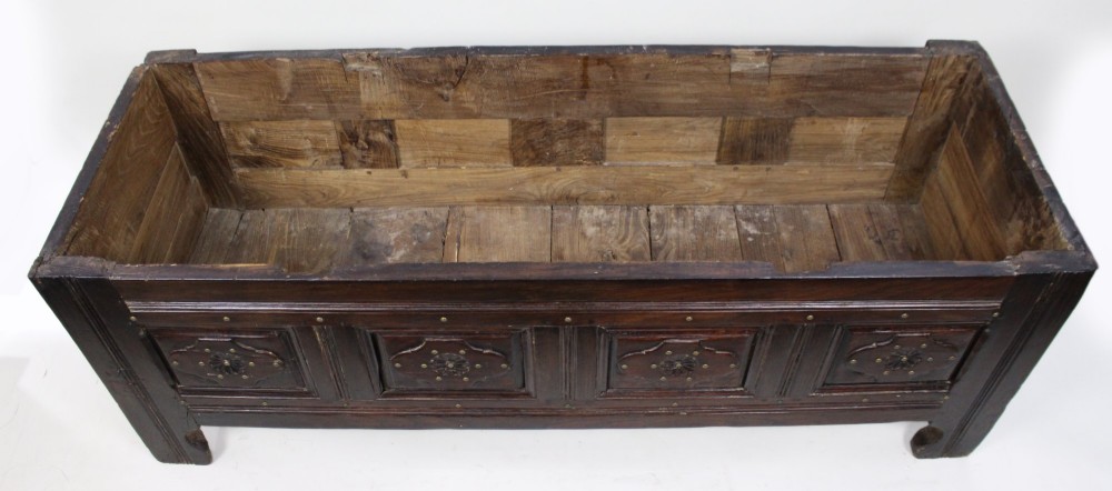 A low rectangular dark oak coffer with a plank lid and four carved recessed panels accented with brass studs. View XIII
