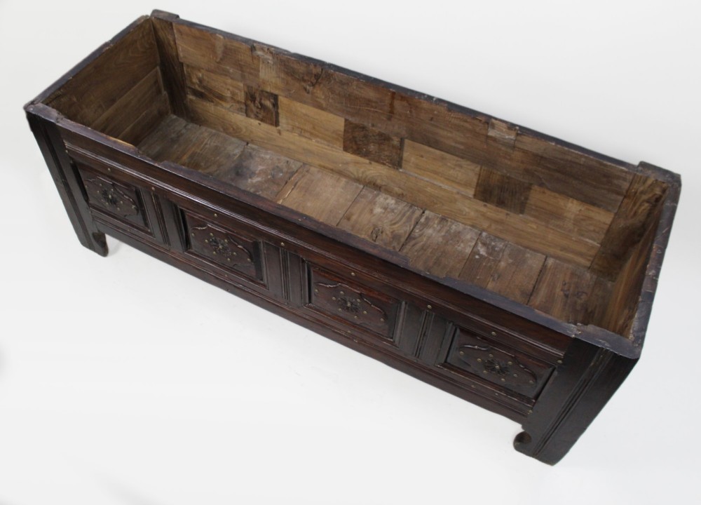 A low rectangular dark oak coffer with a plank lid and four carved recessed panels accented with brass studs. View XIV