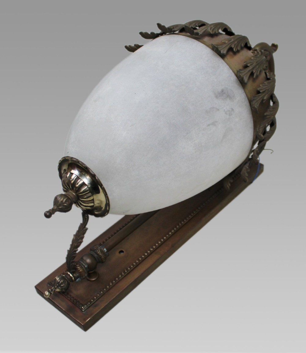 An antique brass wall lantern featuring a frosted ovoid glass shade draped with cast acanthus leaves and topped with a decorative cresting collar. View II