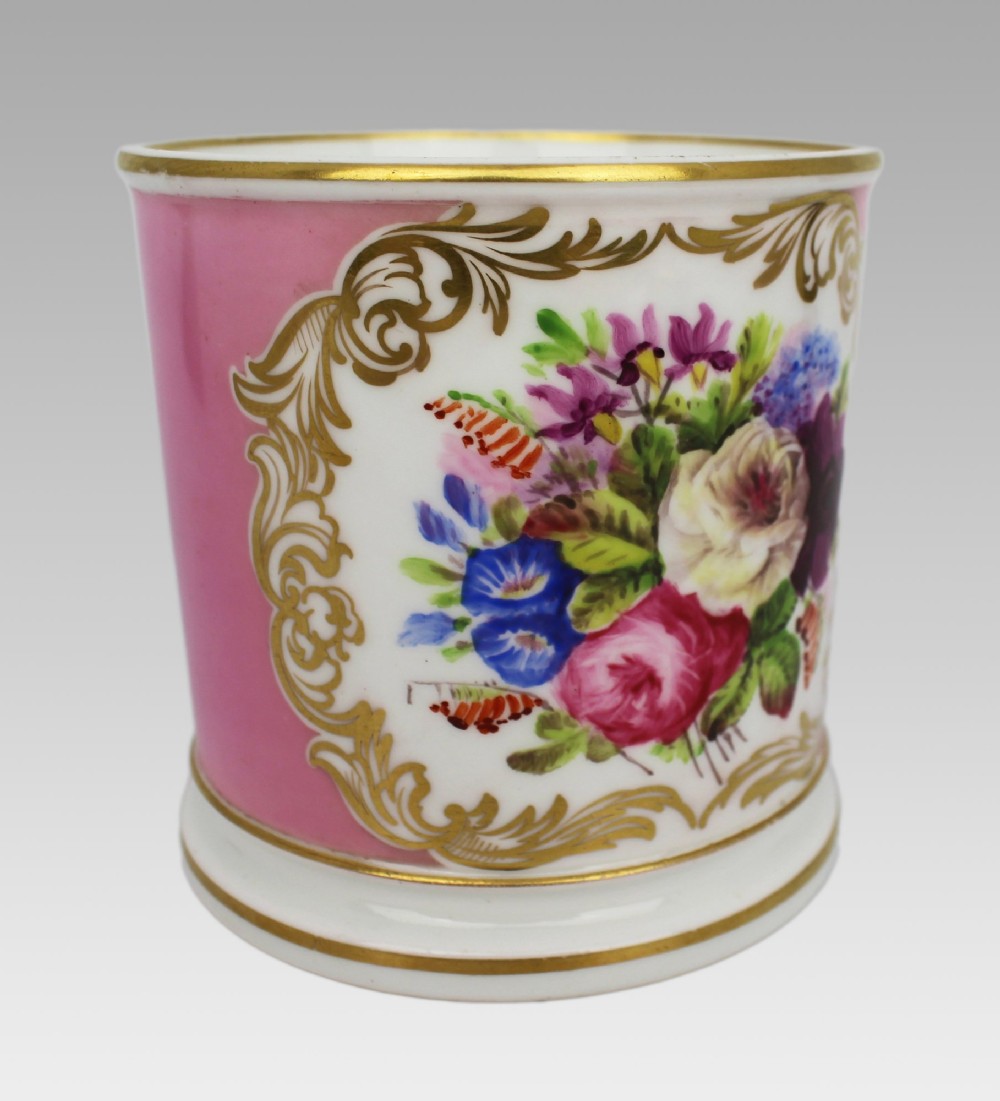 A mid-19th century cylindrical porcelain tankard featuring a Rose Pompadour pink ground, a gilded rococo scroll cartouche with hand-painted flowers, and a gilded handle. View VII