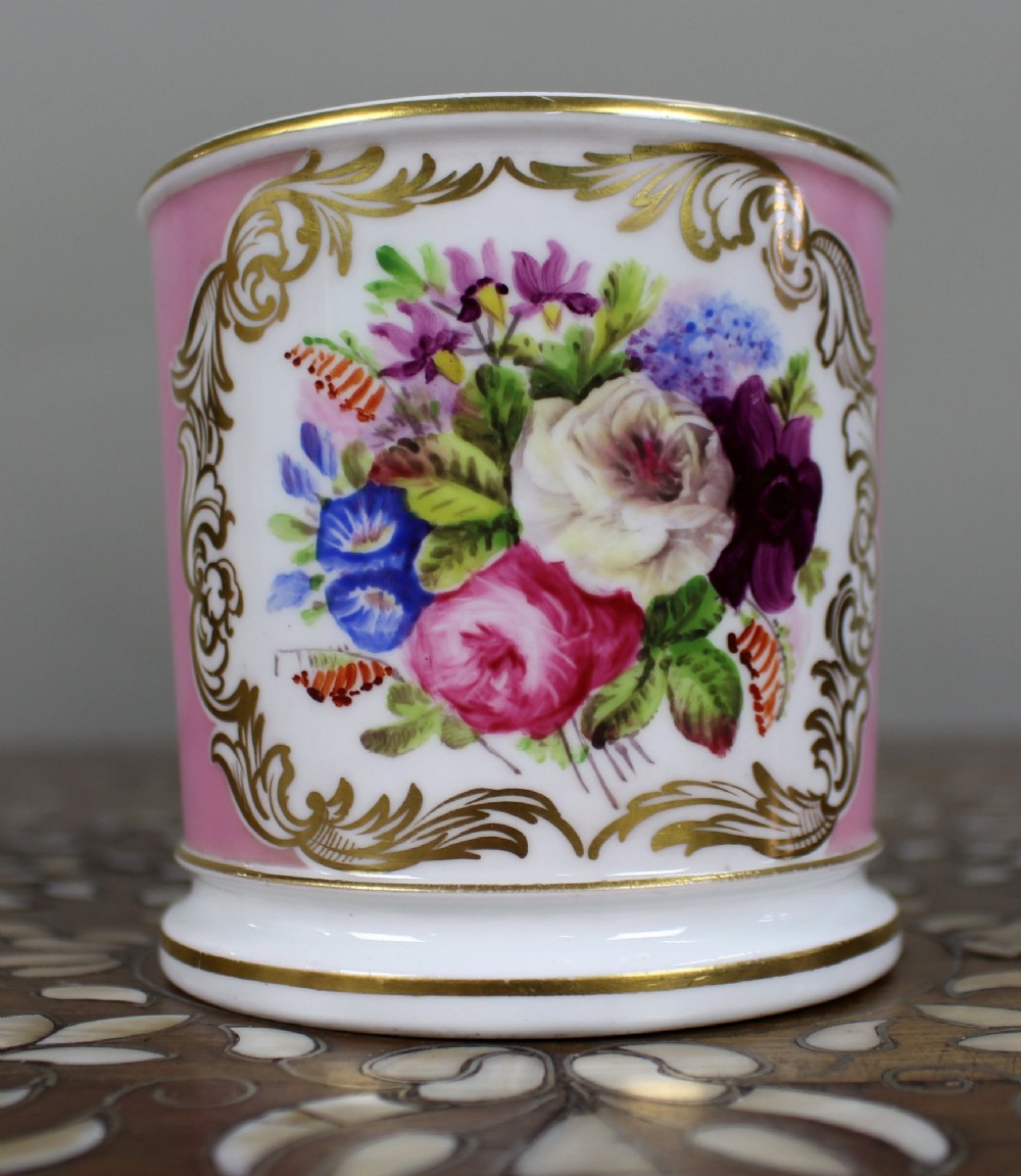 A mid-19th century cylindrical porcelain tankard featuring a Rose Pompadour pink ground, a gilded rococo scroll cartouche with hand-painted flowers, and a gilded handle. View XI