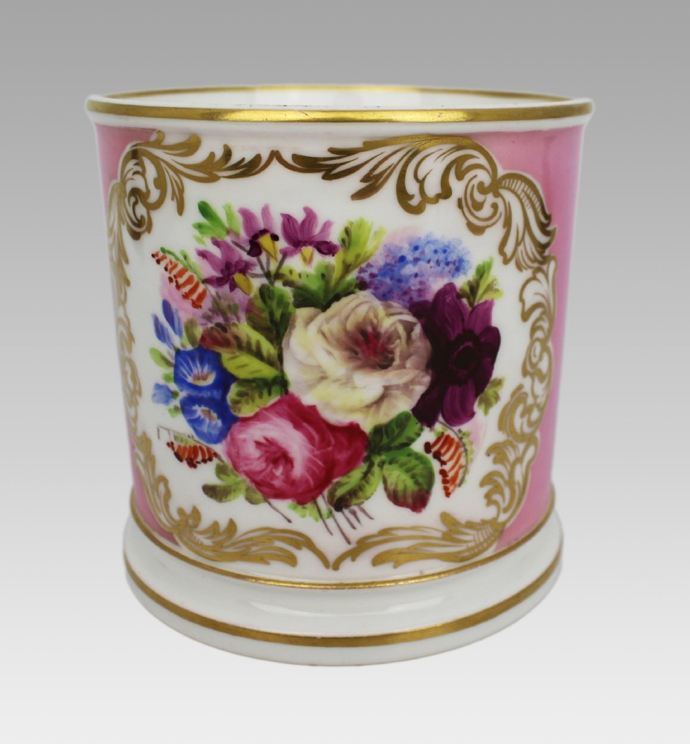A mid-19th century cylindrical porcelain tankard featuring a Rose Pompadour pink ground, a gilded rococo scroll cartouche with hand-painted flowers, and a gilded handle. View XII