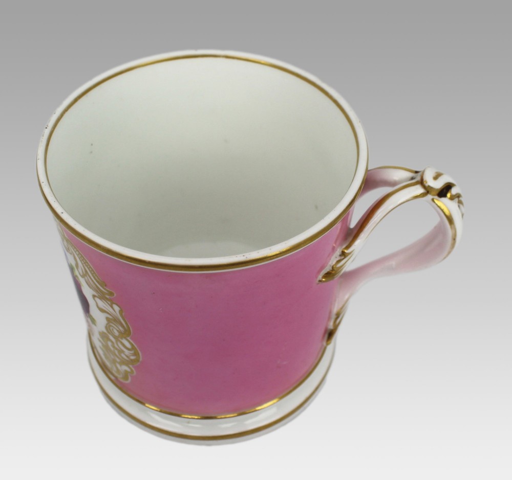 A mid-19th century cylindrical porcelain tankard featuring a Rose Pompadour pink ground, a gilded rococo scroll cartouche with hand-painted flowers, and a gilded handle. View XIV