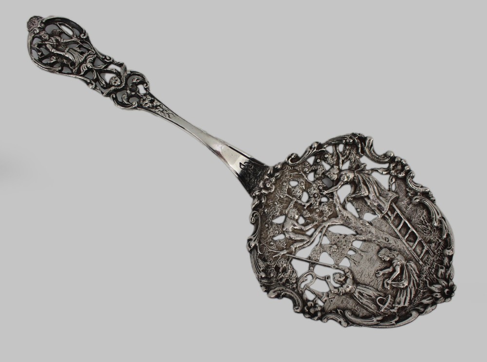 An antique Flemish silver spoon featuring an intricately pierced bowl decorated with a figurative orchard scene and a scrolling openwork handle.