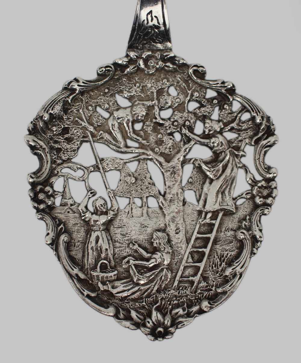 An antique Flemish silver spoon featuring an intricately pierced bowl decorated with a figurative orchard scene and a scrolling openwork handle. View IV