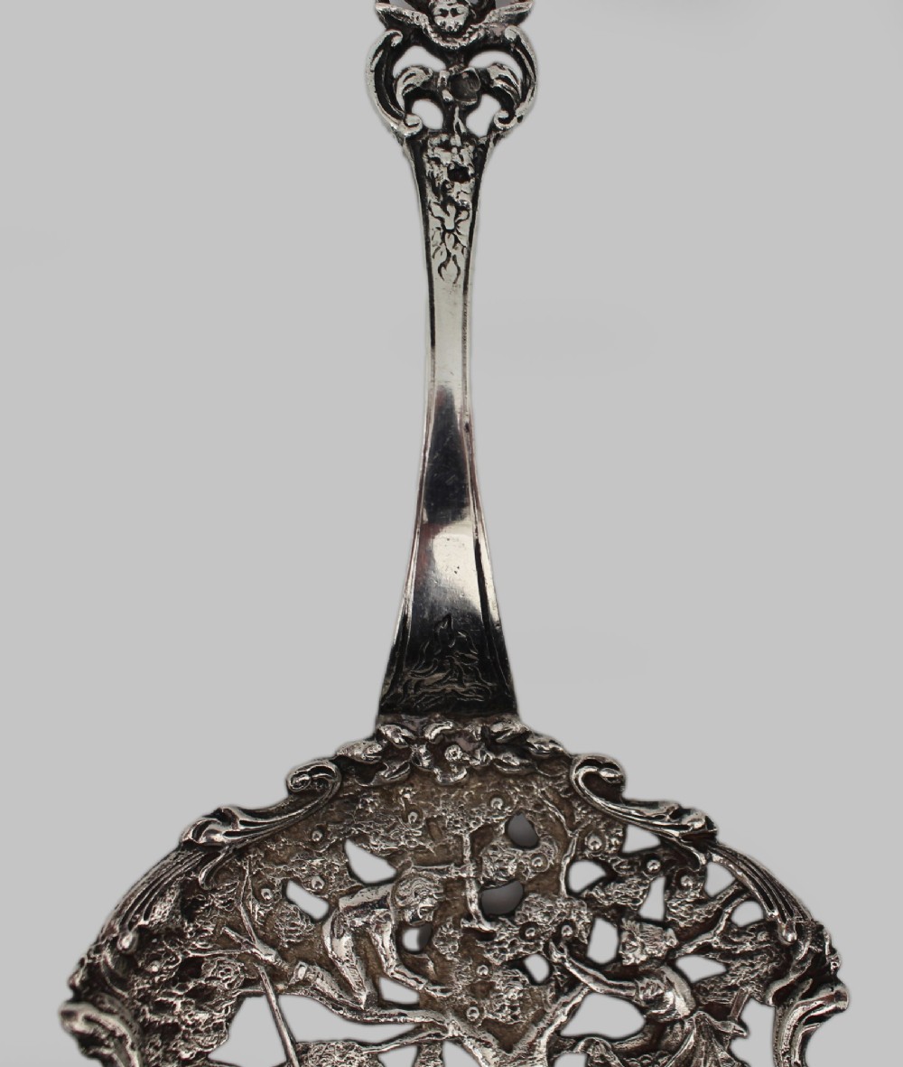An antique Flemish silver spoon featuring an intricately pierced bowl decorated with a figurative orchard scene and a scrolling openwork handle. View V