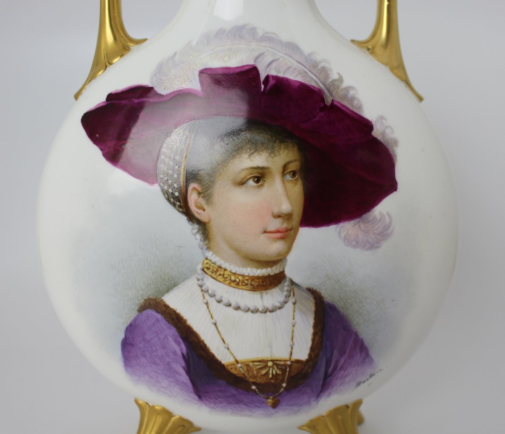 A white porcelain moon flask vase with twin gilded handles, four scroll feet, and a hand-painted portrait of a woman in a purple hat signed Baston. View X