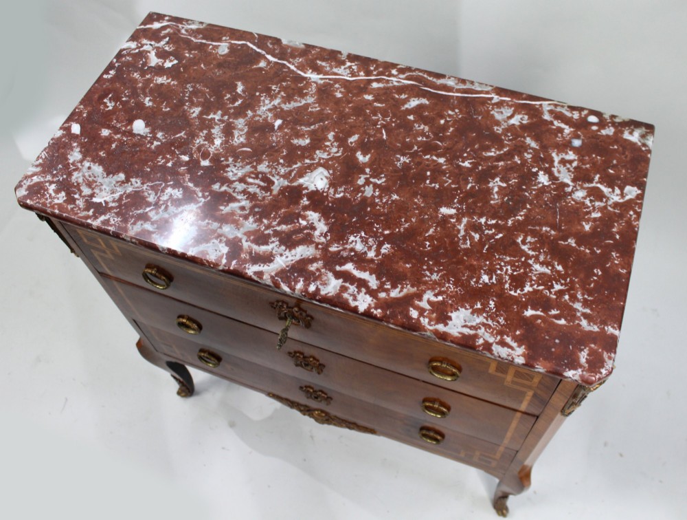 A French Louis XVI style timber commode featuring three drawers with geometric inlaid veneer, gilt-bronze ring handles, and a red variegated marble top. View VI