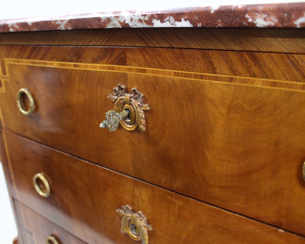 A French Louis XVI style timber commode featuring three drawers with geometric inlaid veneer, gilt-bronze ring handles, and a red variegated marble top. View X