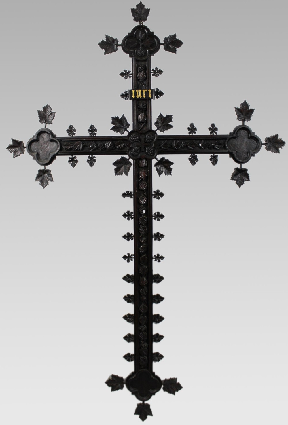 A 19th-century dark carved wood cross adorned with detailed foliate motifs and a gilt INRI inscription at the upper section.