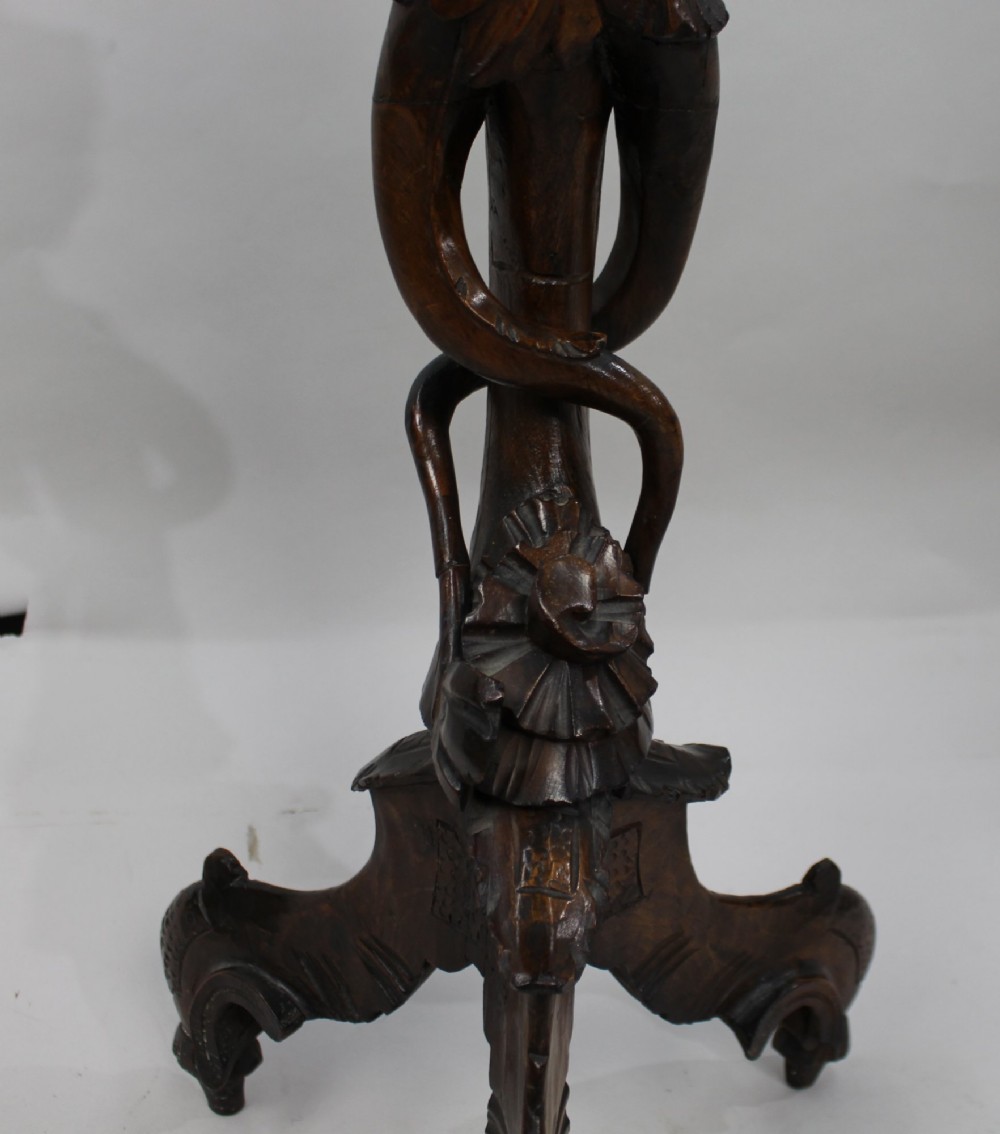 An antique dark carved wood figural pedestal featuring a central figure holding grapes supported on a tripod base with a circular scalloped top. View VI