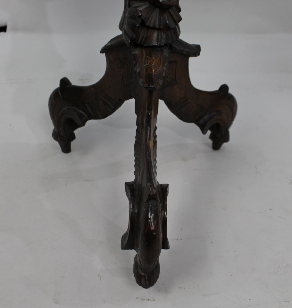 An antique dark carved wood figural pedestal featuring a central figure holding grapes supported on a tripod base with a circular scalloped top. View VII