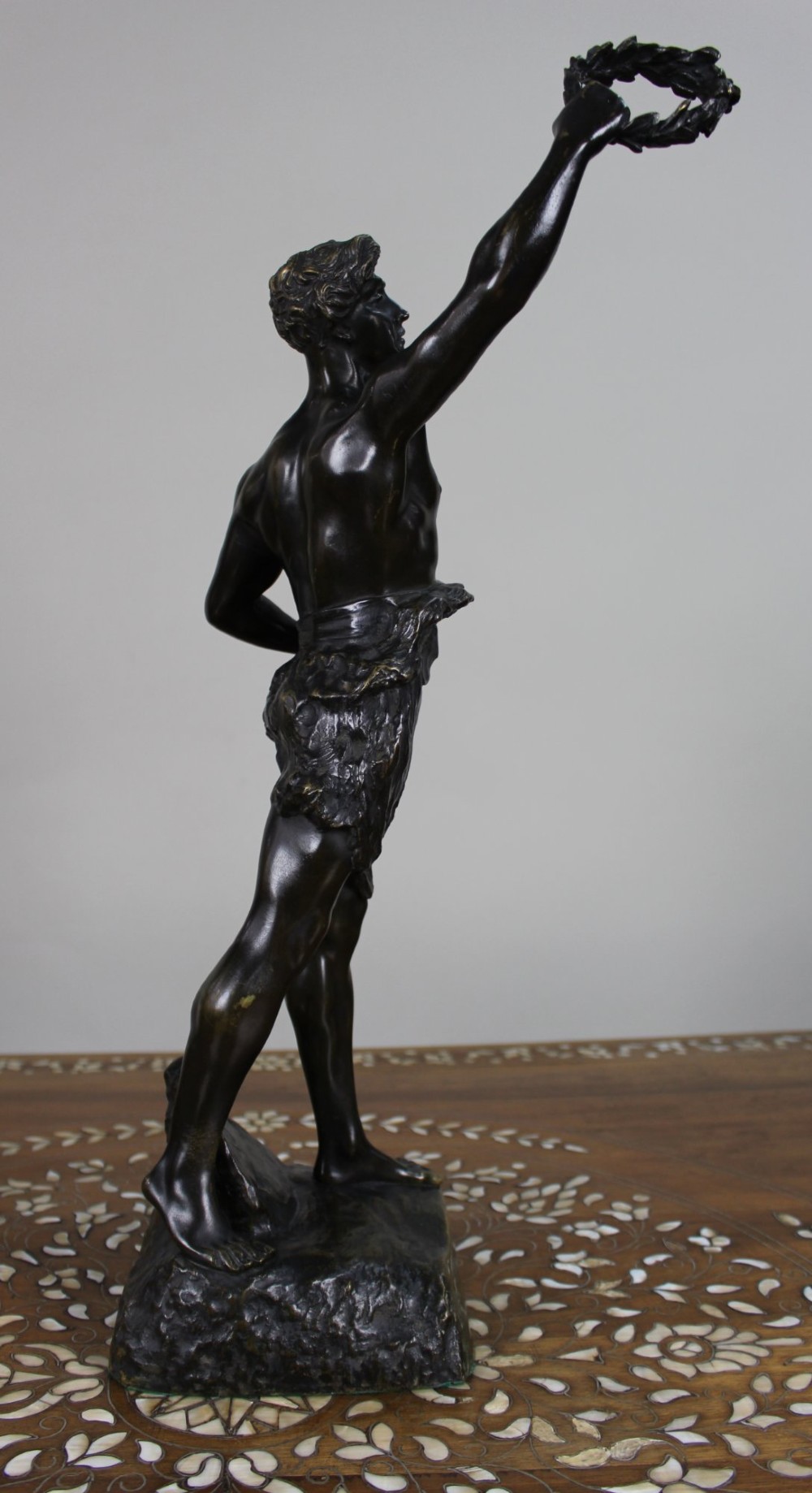 A dark patinated bronze figure of a classical male holding a raised wreath in one hand and a vessel in the other. View III