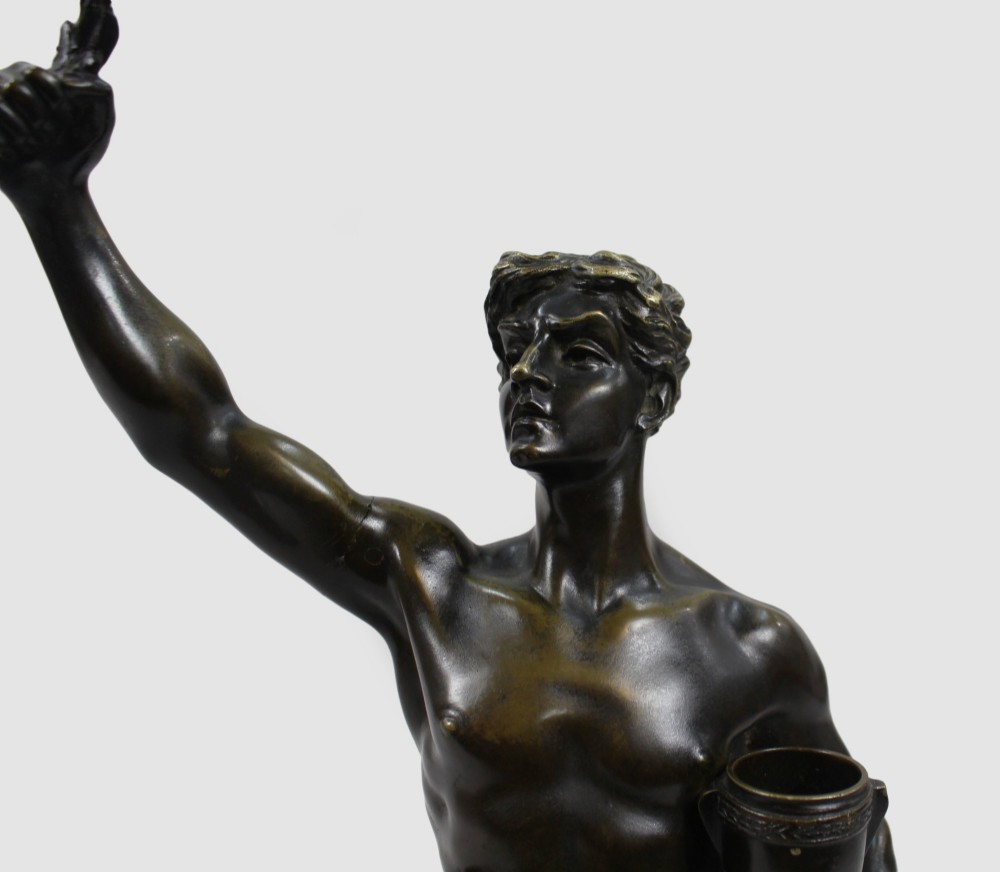 A dark patinated bronze figure of a classical male holding a raised wreath in one hand and a vessel in the other. View XIII