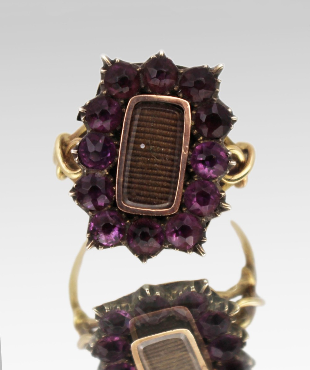 A Victorian yellow gold mourning ring featuring a central rectangular hair compartment surrounded by a halo of faceted purple glass stones.