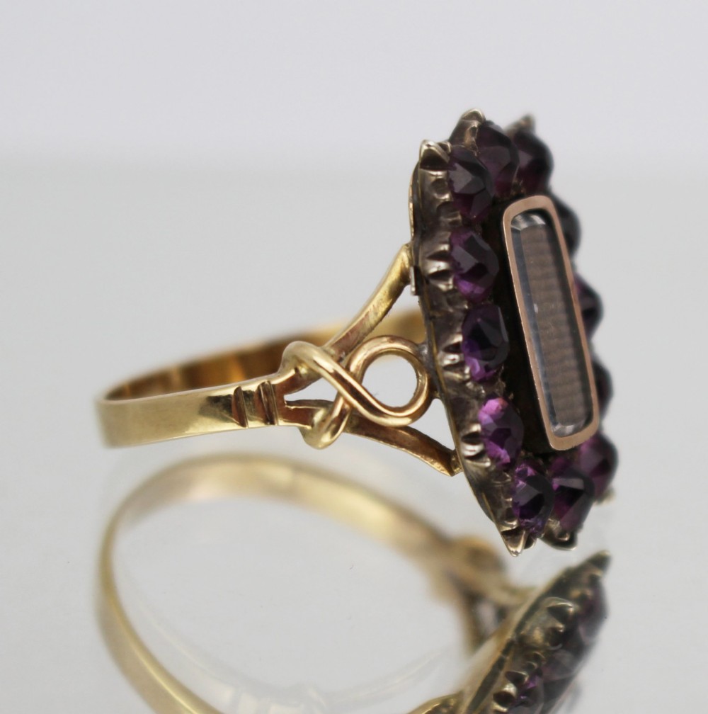 A Victorian yellow gold mourning ring featuring a central rectangular hair compartment surrounded by a halo of faceted purple glass stones. View V