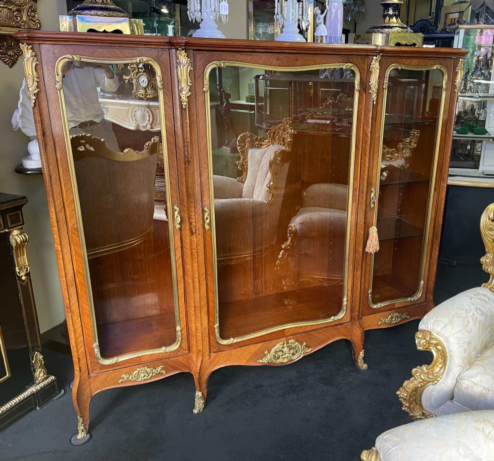 A large French kingwood display cabinet featuring three glass doors, gilded bronze mounts, and cabriole legs. View VIII