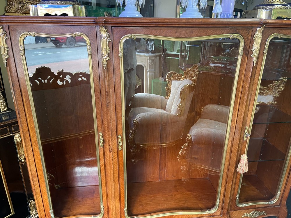 A large French kingwood display cabinet featuring three glass doors, gilded bronze mounts, and cabriole legs. View IX