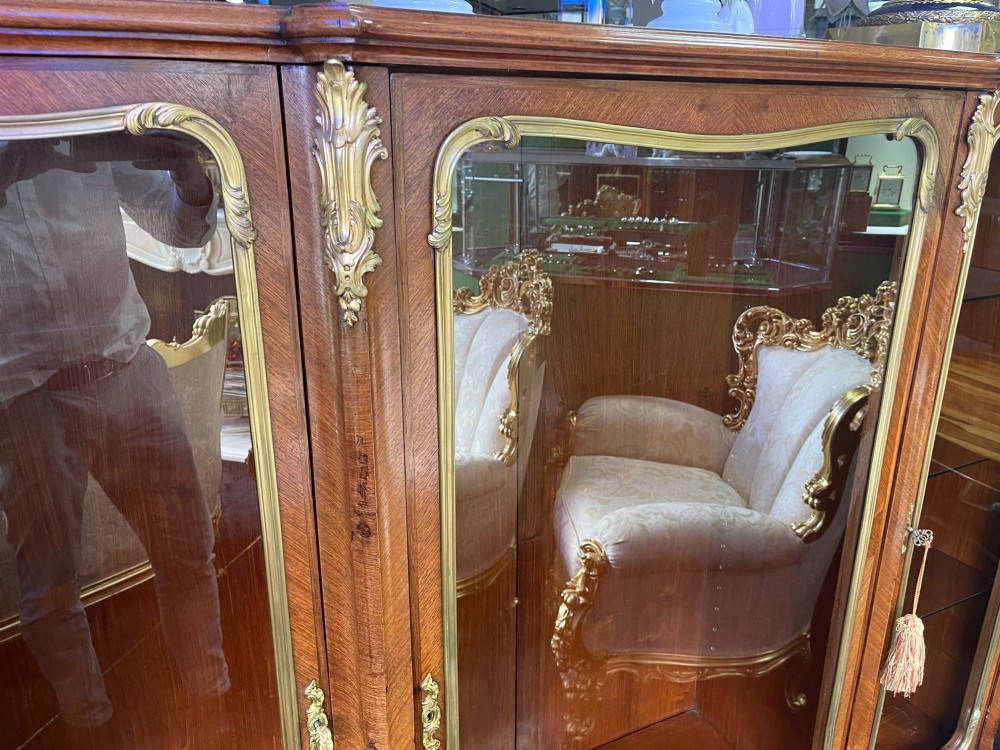 A large French kingwood display cabinet featuring three glass doors, gilded bronze mounts, and cabriole legs. View X