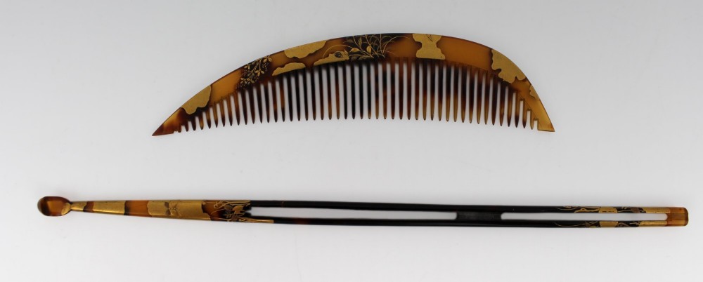 A two-piece Japanese hair ornament set comprising a crescent comb and a slender pin, crafted from mottled amber tortoiseshell with gold lacquer botanical motifs.