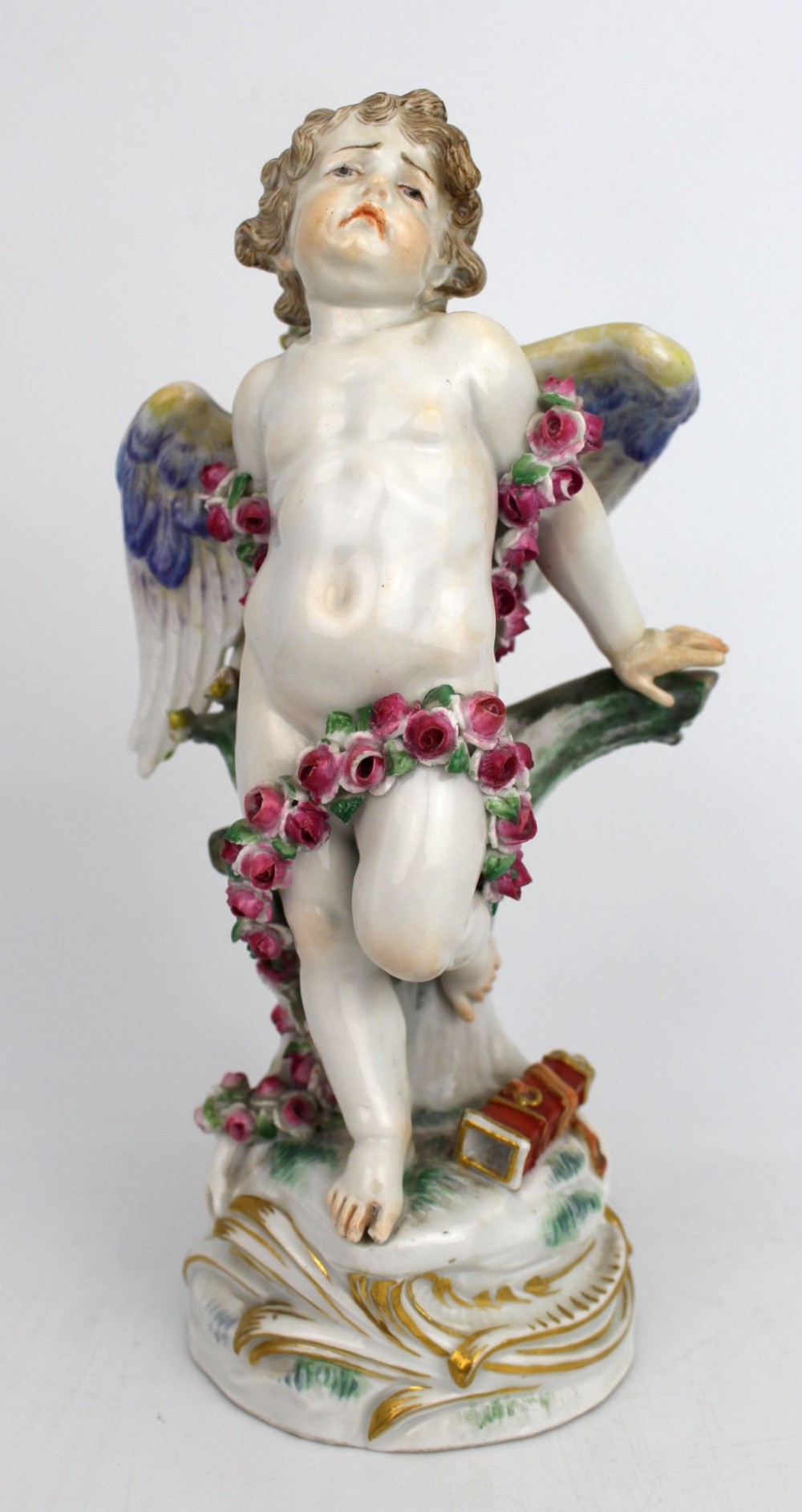 A Meissen hard-paste porcelain figurine depicting a winged cupid bound with a pink rose garland, standing on a gilded scrollwork base.