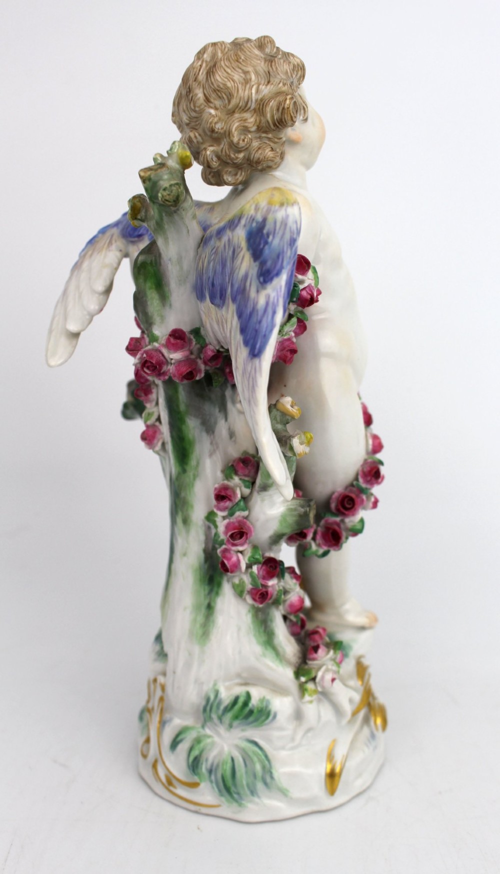 A Meissen hard-paste porcelain figurine depicting a winged cupid bound with a pink rose garland, standing on a gilded scrollwork base. View III