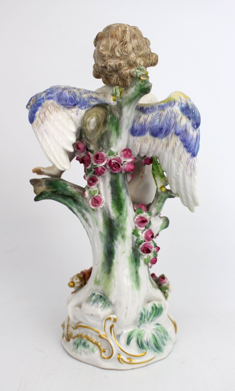 A Meissen hard-paste porcelain figurine depicting a winged cupid bound with a pink rose garland, standing on a gilded scrollwork base. View IV