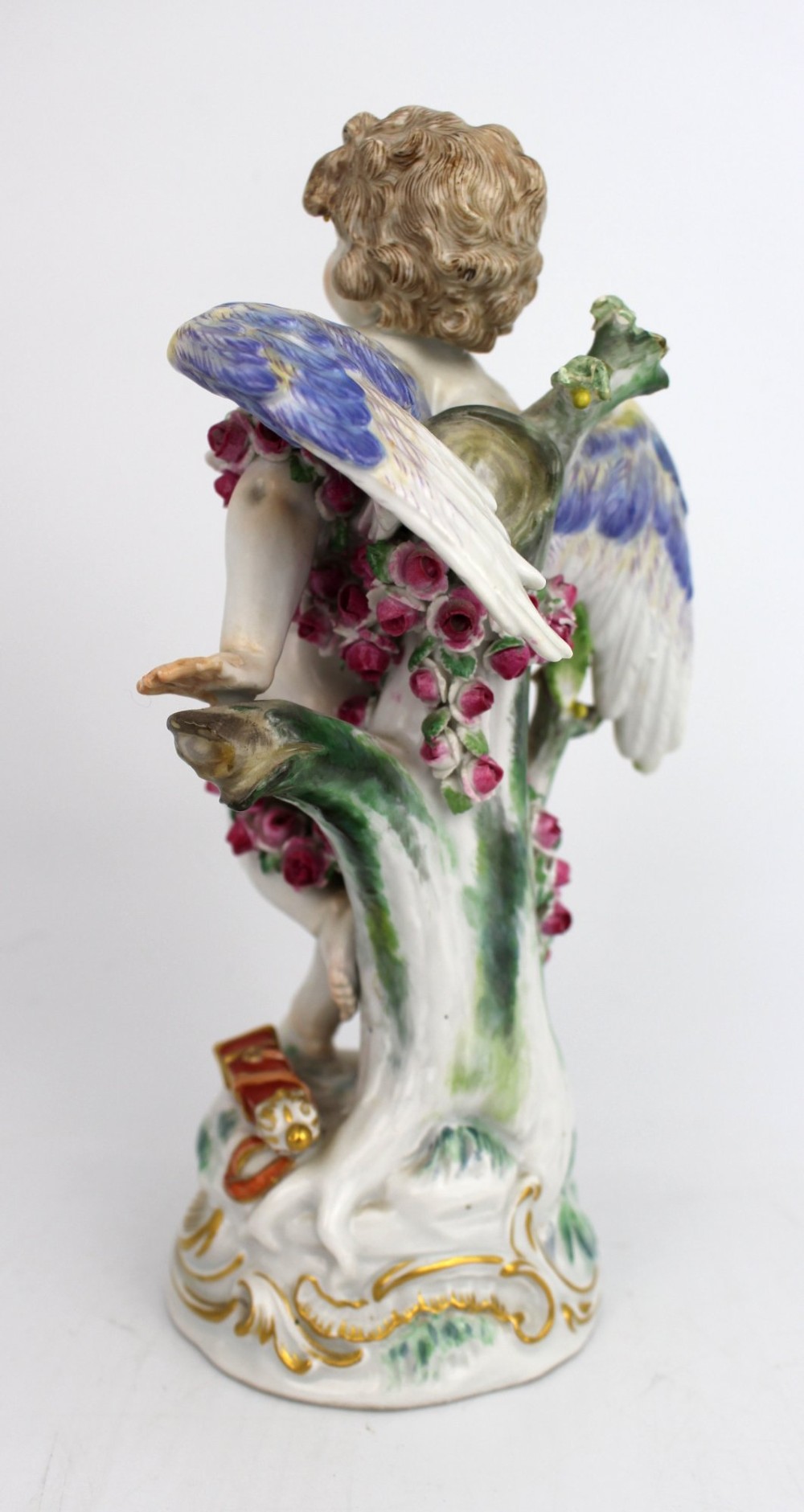 A Meissen hard-paste porcelain figurine depicting a winged cupid bound with a pink rose garland, standing on a gilded scrollwork base. View V