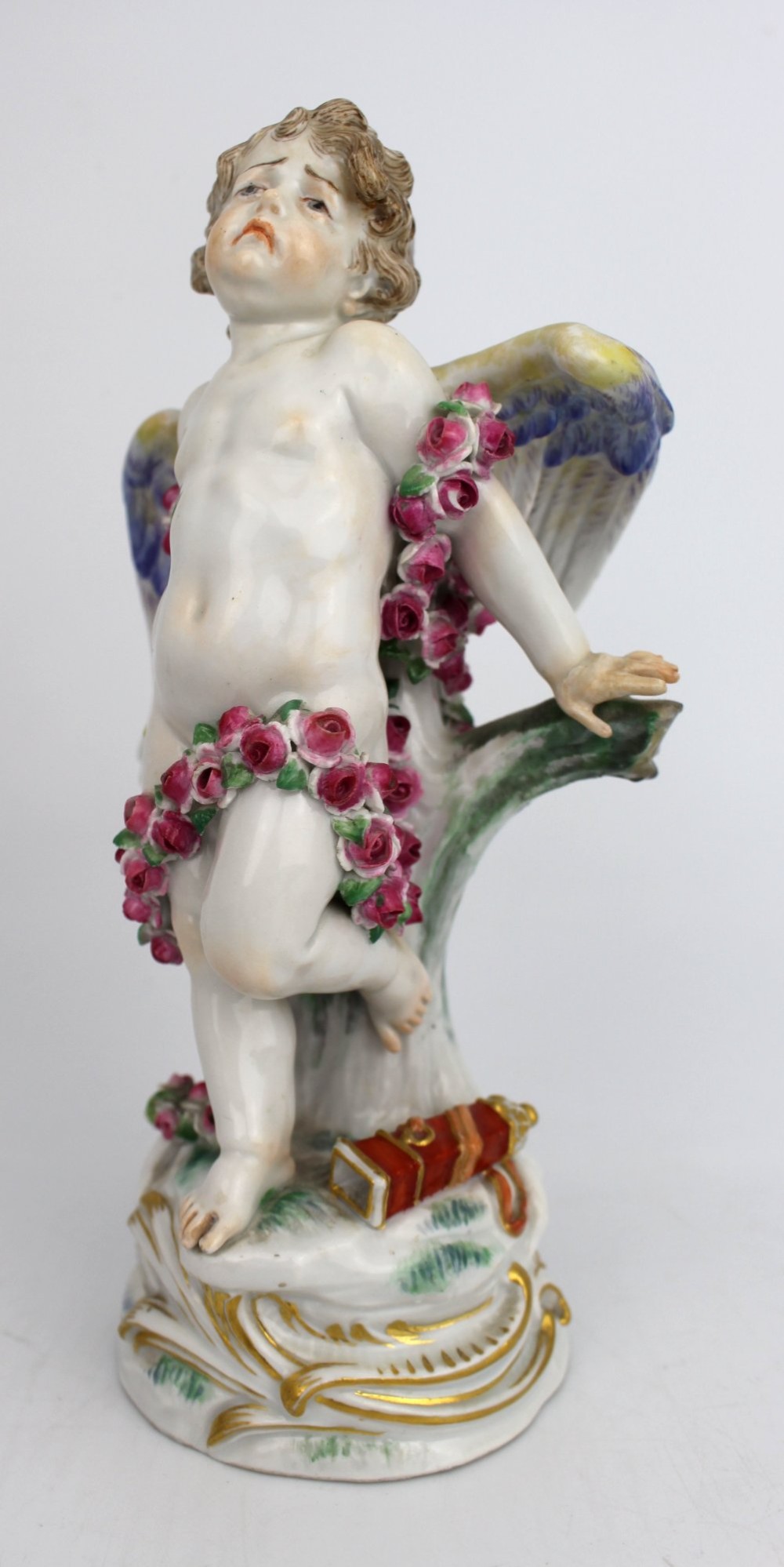 A Meissen hard-paste porcelain figurine depicting a winged cupid bound with a pink rose garland, standing on a gilded scrollwork base. View VII