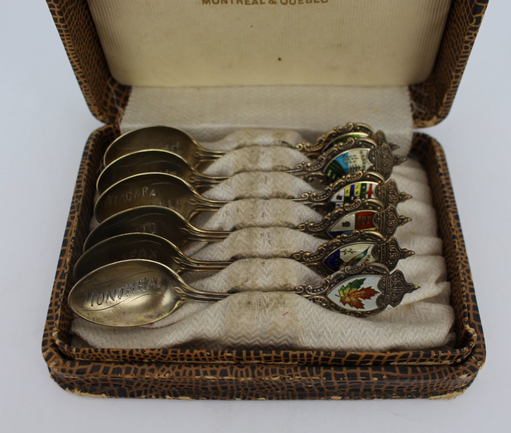 A cased set of six sterling silver demitasse spoons featuring colourful enamelled crest finials set inside a textured brown presentation box. View II
