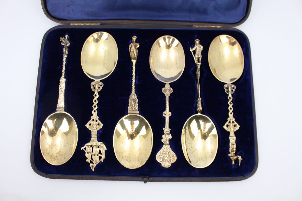 A set of six silver-gilt apostle spoons with cast figural finials and decorative shanks presented inside a dark blue velvet-lined fitted display case. View II