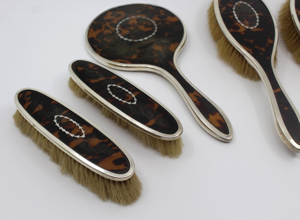 A five-piece Art Deco sterling silver and faux tortoiseshell vanity set featuring a hand mirror, two handled hairbrushes, and two clothes brushes with silver leaf-wreath inlays. View II