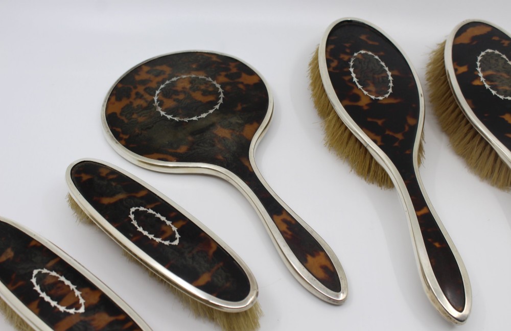 A five-piece Art Deco sterling silver and faux tortoiseshell vanity set featuring a hand mirror, two handled hairbrushes, and two clothes brushes with silver leaf-wreath inlays. View III