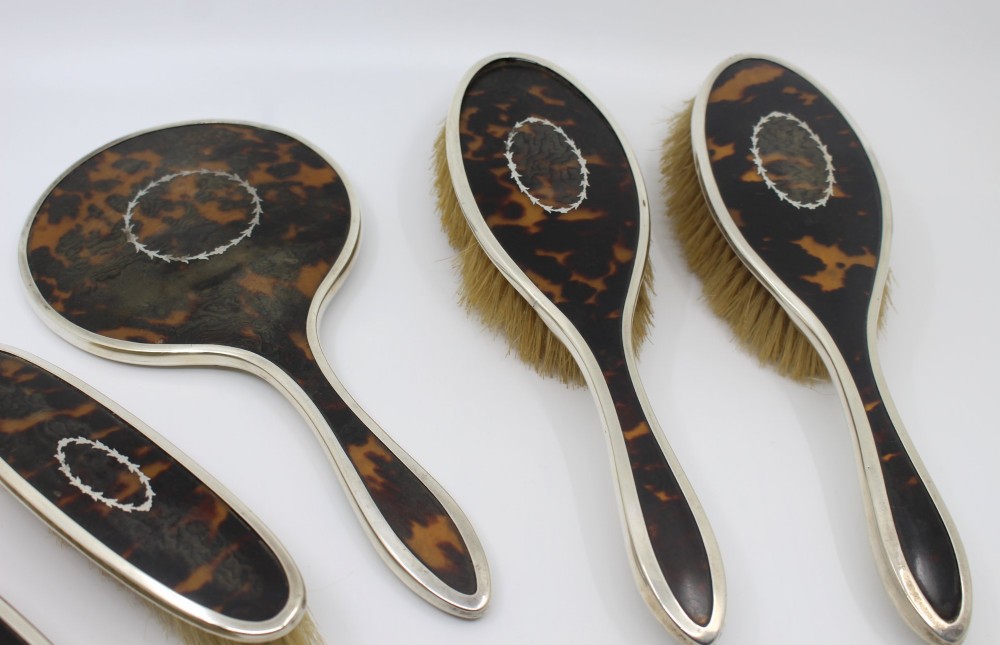 A five-piece Art Deco sterling silver and faux tortoiseshell vanity set featuring a hand mirror, two handled hairbrushes, and two clothes brushes with silver leaf-wreath inlays. View IV