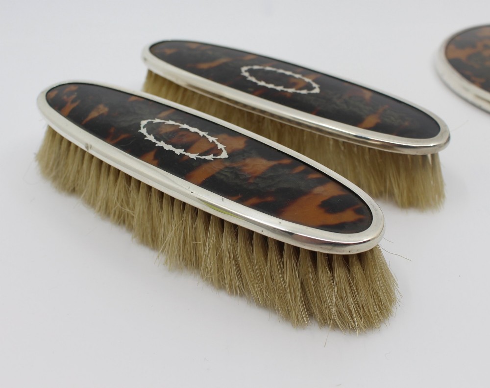 A five-piece Art Deco sterling silver and faux tortoiseshell vanity set featuring a hand mirror, two handled hairbrushes, and two clothes brushes with silver leaf-wreath inlays. View V
