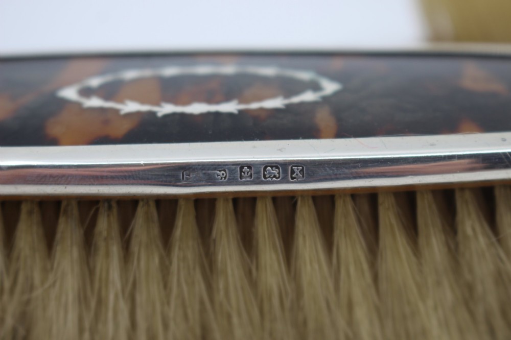 A five-piece Art Deco sterling silver and faux tortoiseshell vanity set featuring a hand mirror, two handled hairbrushes, and two clothes brushes with silver leaf-wreath inlays. View VII