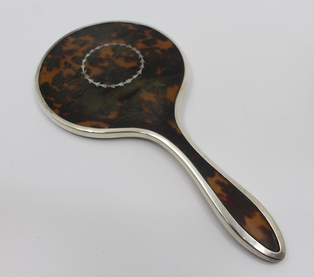 A five-piece Art Deco sterling silver and faux tortoiseshell vanity set featuring a hand mirror, two handled hairbrushes, and two clothes brushes with silver leaf-wreath inlays. View VIII