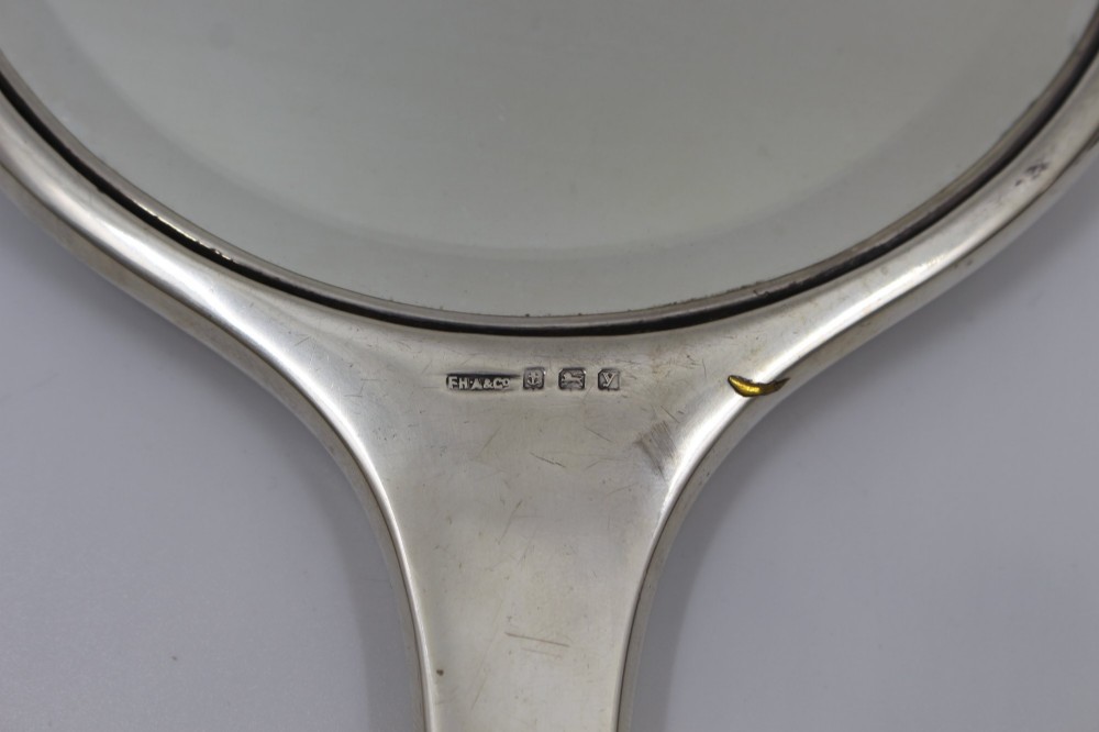 A five-piece Art Deco sterling silver and faux tortoiseshell vanity set featuring a hand mirror, two handled hairbrushes, and two clothes brushes with silver leaf-wreath inlays. View X