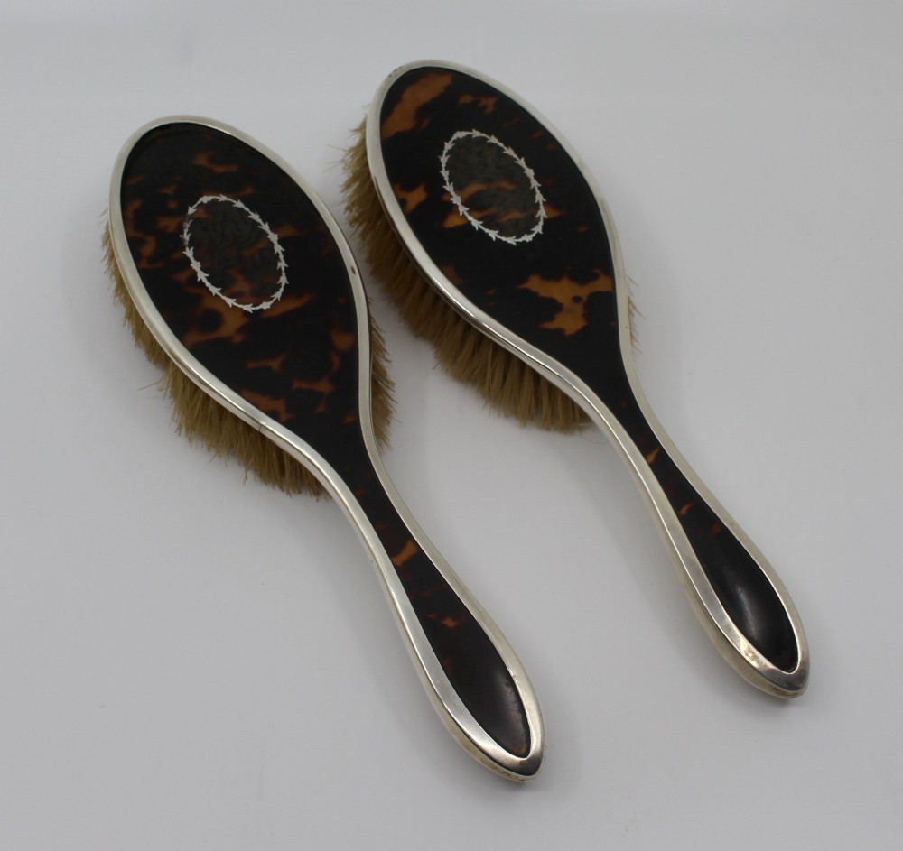 A five-piece Art Deco sterling silver and faux tortoiseshell vanity set featuring a hand mirror, two handled hairbrushes, and two clothes brushes with silver leaf-wreath inlays. View XI