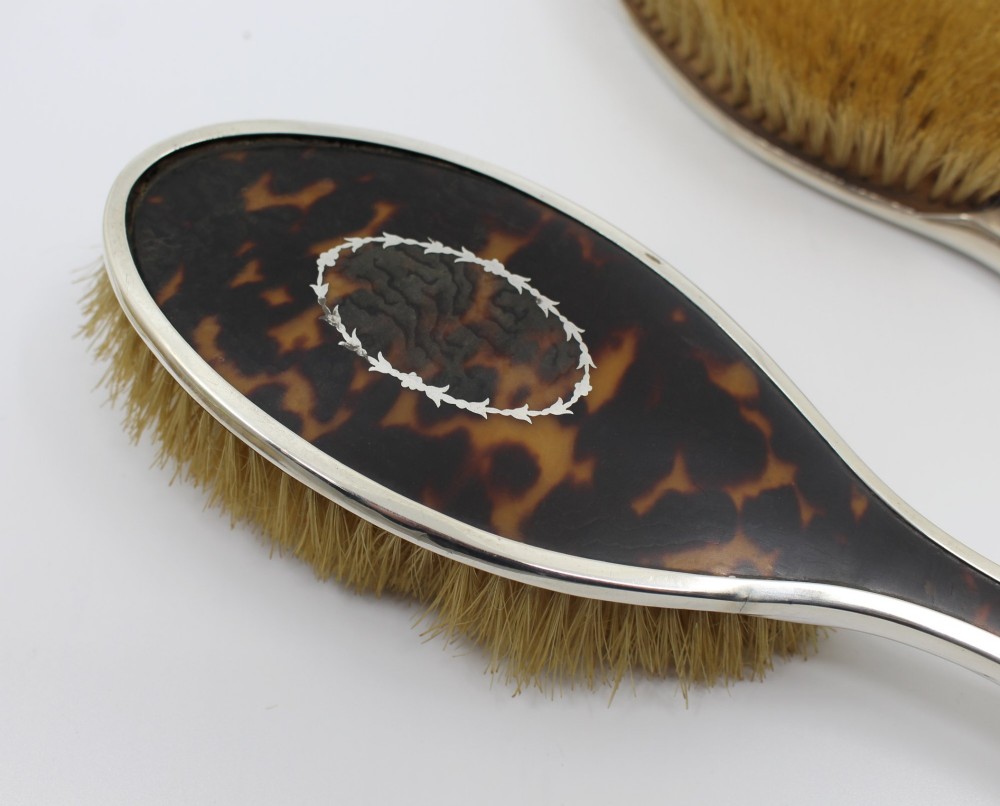 A five-piece Art Deco sterling silver and faux tortoiseshell vanity set featuring a hand mirror, two handled hairbrushes, and two clothes brushes with silver leaf-wreath inlays. View XII
