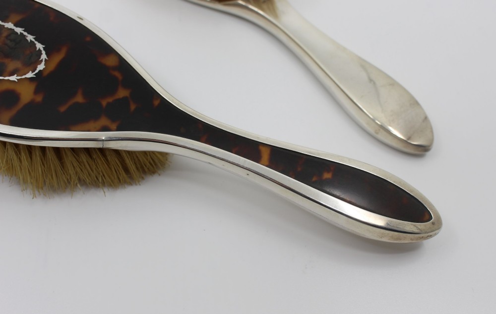 A five-piece Art Deco sterling silver and faux tortoiseshell vanity set featuring a hand mirror, two handled hairbrushes, and two clothes brushes with silver leaf-wreath inlays. View XIII