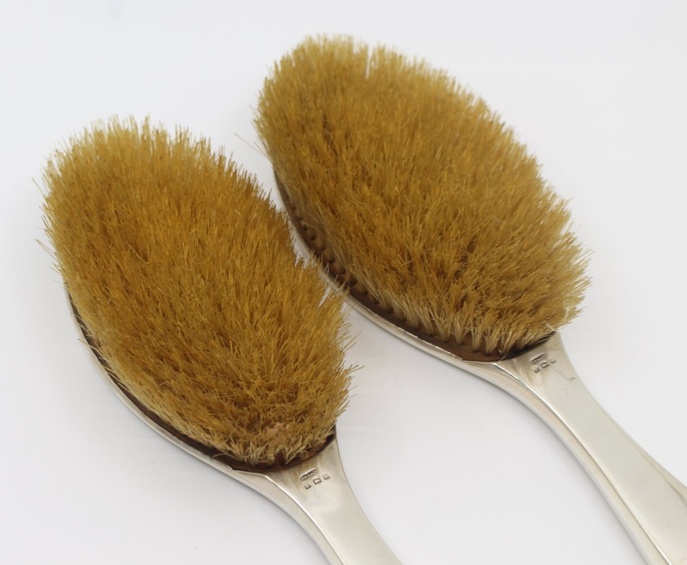 A five-piece Art Deco sterling silver and faux tortoiseshell vanity set featuring a hand mirror, two handled hairbrushes, and two clothes brushes with silver leaf-wreath inlays. View XV