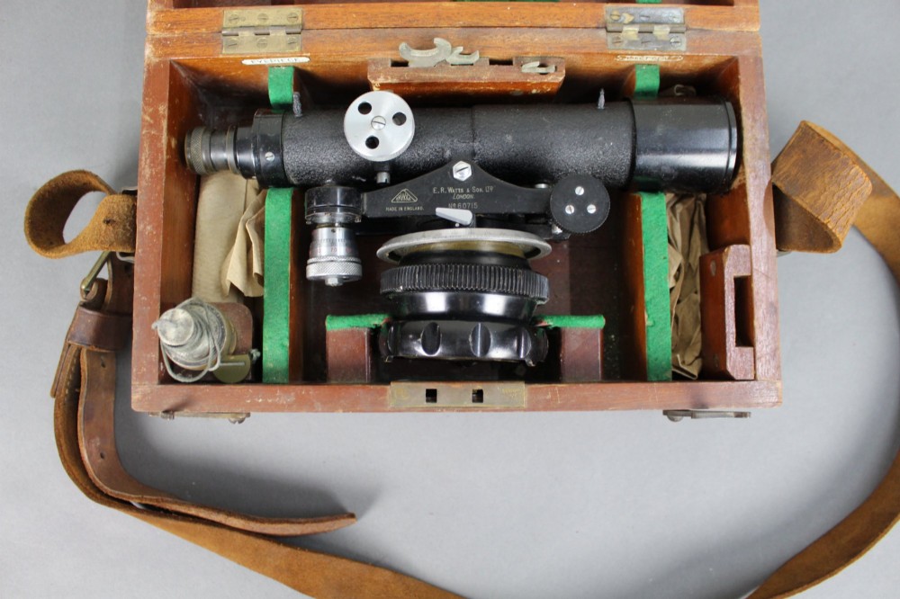 A vintage black metal surveyor level set inside its original fitted wooden transport box with a leather strap and manufacturer label. View II