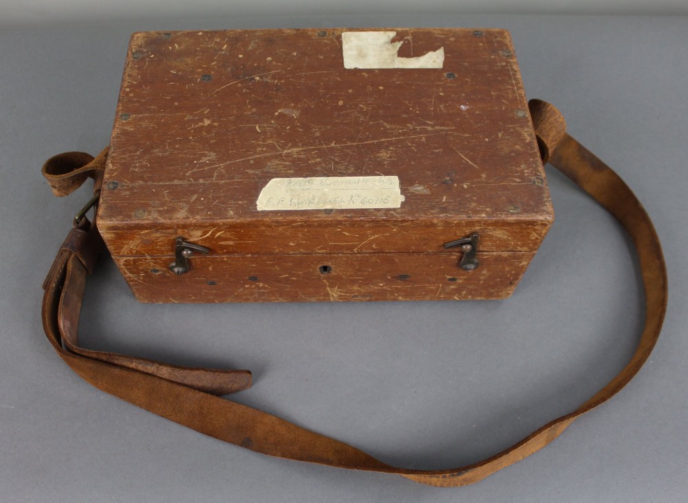 A vintage black metal surveyor level set inside its original fitted wooden transport box with a leather strap and manufacturer label. View VIII
